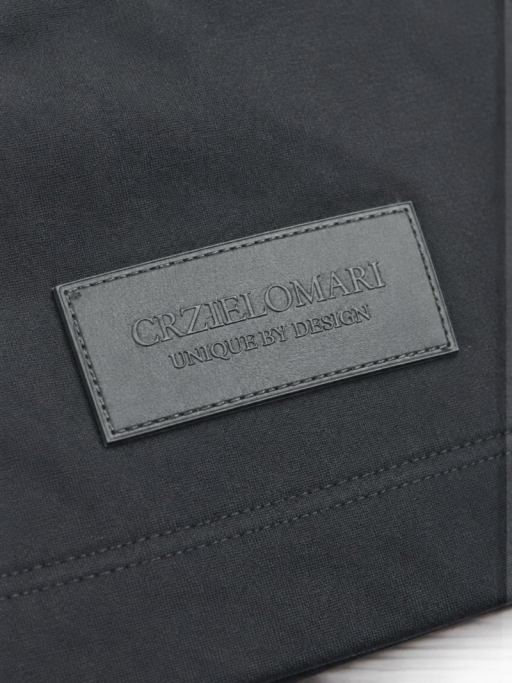 Close-up of the tonal CRZELOMARI patch on the hem of The Legacy Tee